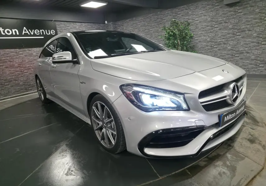 Mercedes CLA Shooting Brake gris, vue 3/4 avant droit avec phares LED allumés et jantes AMG 18 pouces.