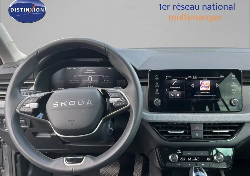 Vue intérieure centrée sur le volant SKODA et l’écran tactile du tableau de bord, ambiance gris noir moderne.