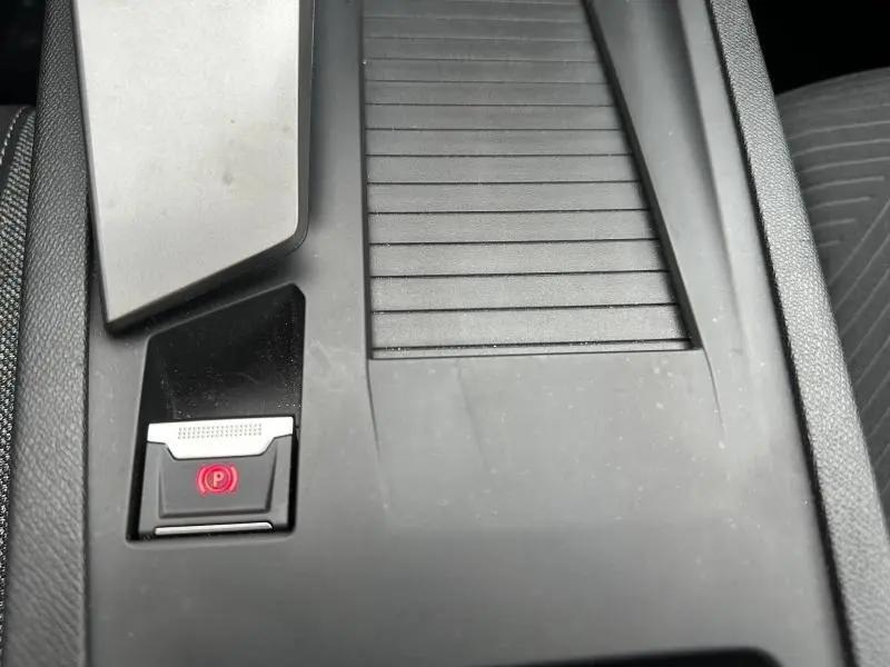 Gros plan sur la console centrale noire du Peugeot 308 2024, avec bouton de frein à main électronique illuminé en rouge.