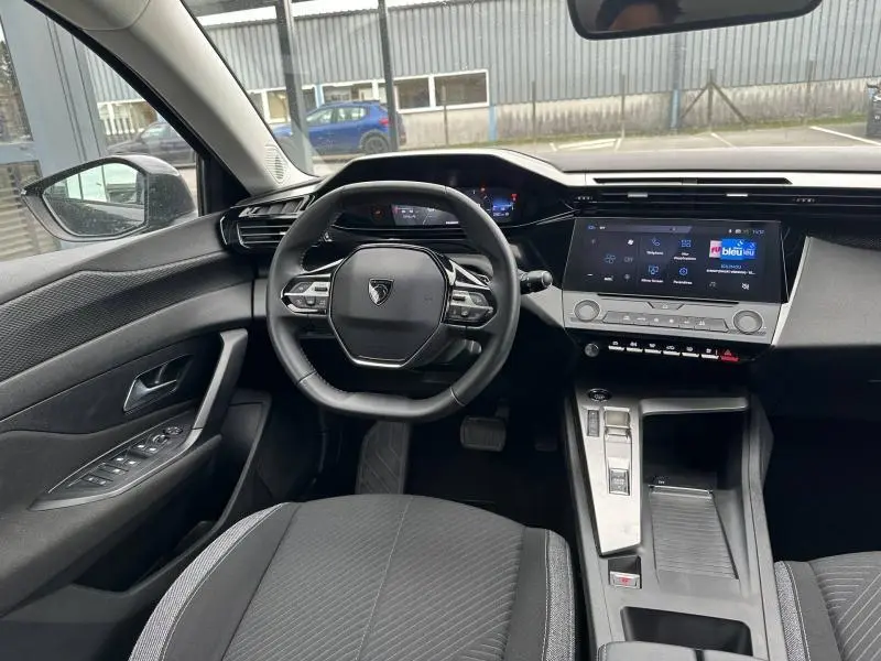 Vue intérieure avant de la Peugeot 308 2024 en Noir Perla Nera, montrant le volant compact et l'écran tactile central.