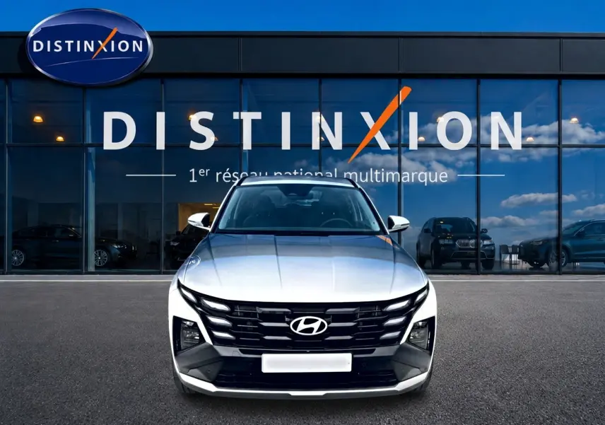 Vue avant d'un Hyundai Tucson blanc 2026 avec calandre noire et logo Hyundai, devant une vitrine Distinxion.