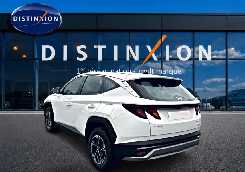 Vue 3/4 arrière droite d'un Hyundai Tucson blanc 2026 hybride devant une vitrine Distinxion.
