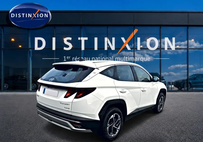 Vue 3/4 arrière droite d'un Hyundai Tucson blanc hybride 2026 avec jantes alliage et feux arrière LED distinctifs.
