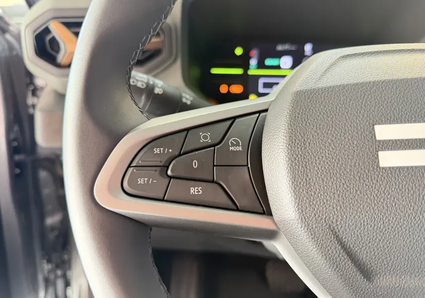 Gros plan sur les commandes du régulateur de vitesse au volant du Dacia Duster Hybrid 155 Extreme, intérieur gris.