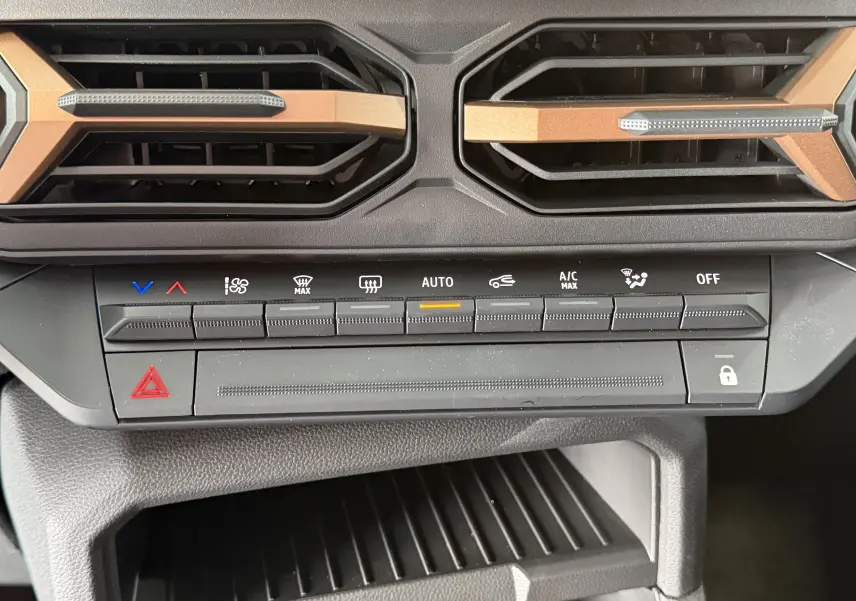 Gros plan sur les commandes de climatisation et les aérateurs noirs avec inserts brun cuivré du Dacia Duster Hybrid 155 Extreme.