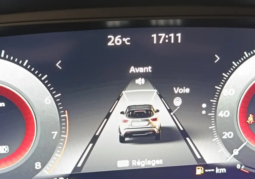 Affichage numérique du tableau de bord montrant une voiture blanche vue de dos sur une route virtuelle, température 26°C, heure 17:11.