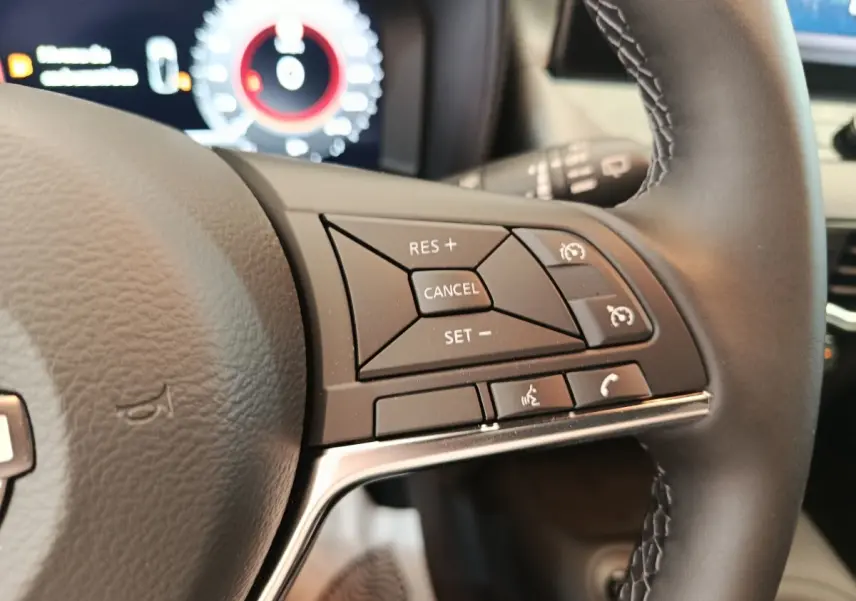Gros plan sur les commandes du régulateur de vitesse au volant cuir noir du Nissan Juke DIG-T 114 BVM6 N-Connecta 2025.