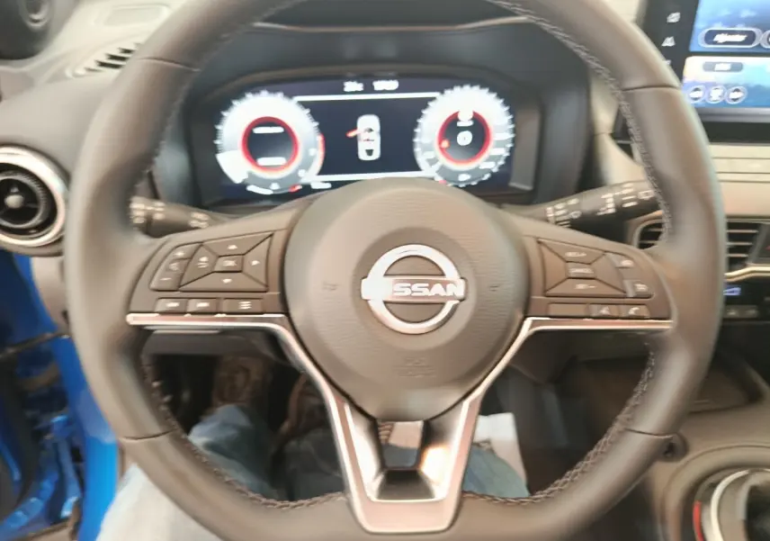 Vue intérieure centrée sur le volant cuir du Nissan Juke bleu 2025 avec tableau de bord numérique et écran tactile.