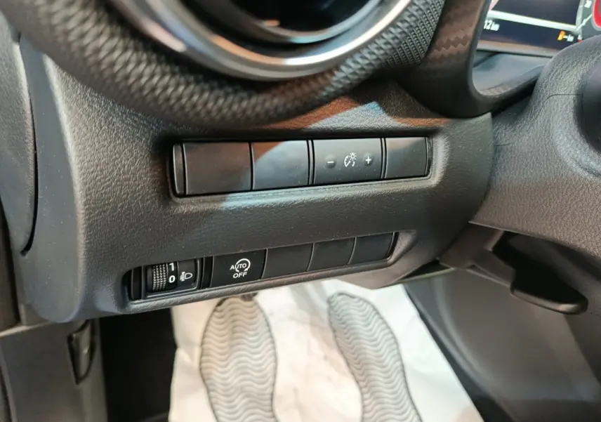 Gros plan sur les commandes d’éclairage et réglage du tableau de bord côté gauche dans l’habitacle noir du Nissan Juke bleu 2025.