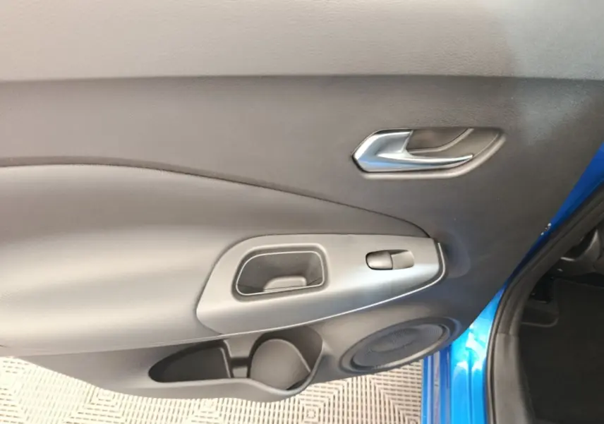 Intérieur côté gauche de la porte avant d’un Nissan Juke bleu 2025, avec poignée argentée et haut-parleur intégré.