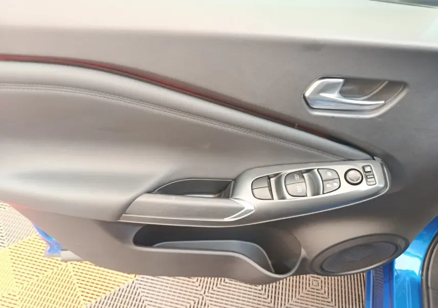 Intérieur de la porte avant gauche du Nissan Juke bleu, avec commandes de vitres et poignée argentée.