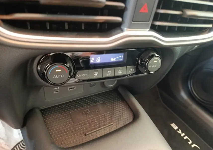 Gros plan sur la console centrale du Nissan Juke 2025, montrant les commandes de climatisation et la zone de recharge sans fil.