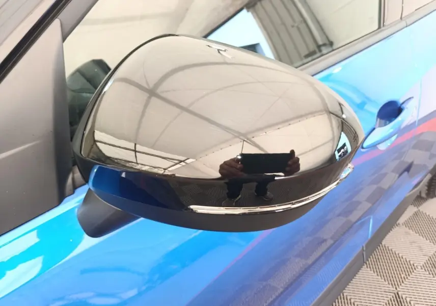 Rétroviseur droit noir brillant sur Nissan Juke bleu, vue rapprochée côté conducteur avec poignée de porte visible.