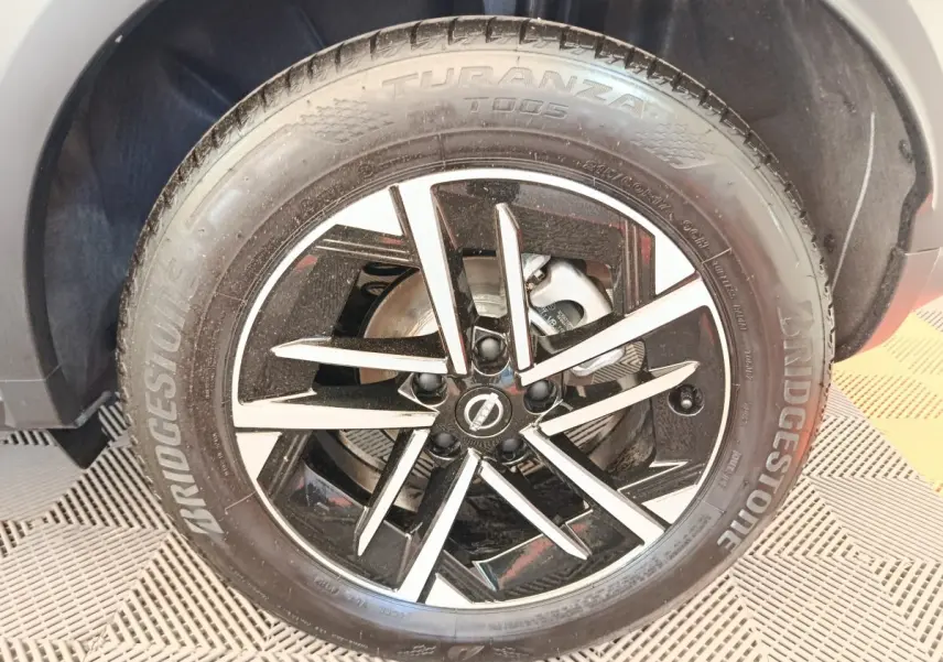 Gros plan sur la roue avant gauche du Nissan Juke bleu 2025, jante alliage noir et argent avec logo Nissan central.