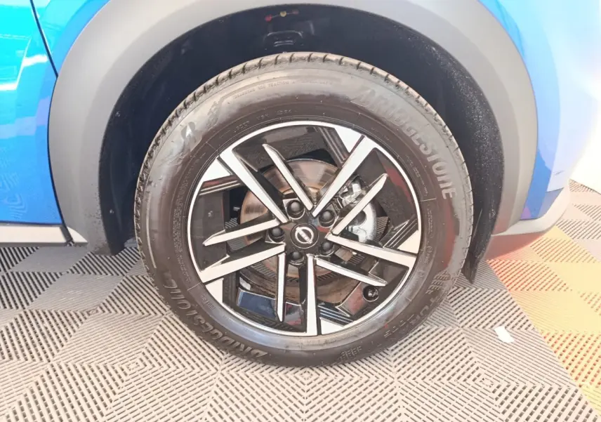 Gros plan sur la roue avant droite du Nissan Juke bleu 2025 avec jante alliage noire et argentée.