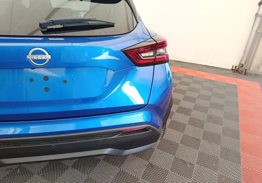 Vue arrière droite d'un Nissan Juke bleu 2025 avec feux LED et pare-chocs noir mat sur sol carrelé.