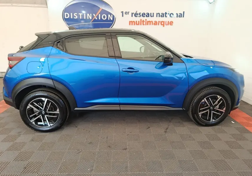 Profil droit d'un Nissan Juke bleu 2025 avec toit noir, jantes alliage noires et détails sportifs visibles.