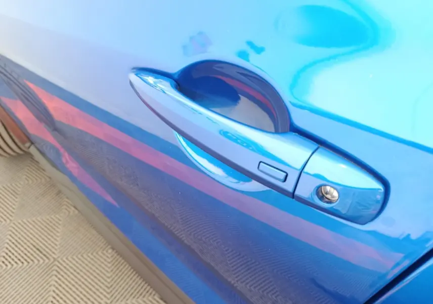 Poignée de porte côté droit bleu vif d'une Nissan Juke 2025 DIG-T 114 BVM6 N-Connecta en gros plan.