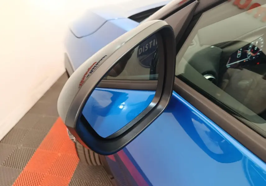Rétroviseur côté gauche en gros plan sur Nissan Juke bleu, avec partie avant et tableau de bord visible.