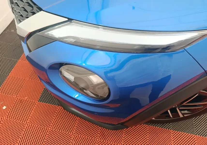Gros plan sur le phare avant droit bleu vif du Nissan Juke 2025 avec détails du pare-chocs noir et calandre.