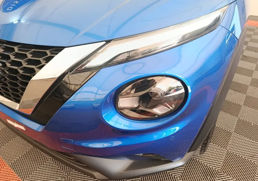 Gros plan sur l'avant droit bleu vif du Nissan Juke 2025, mettant en valeur ses phares LED distinctifs et la calandre noire.