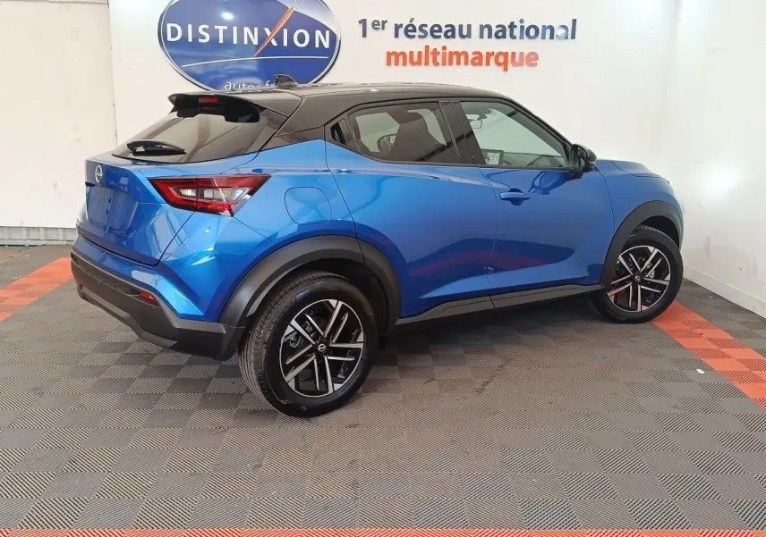 Vue 3/4 arrière droite d'un Nissan Juke bleu 2025 avec toit noir et jantes alliage noires en showroom.