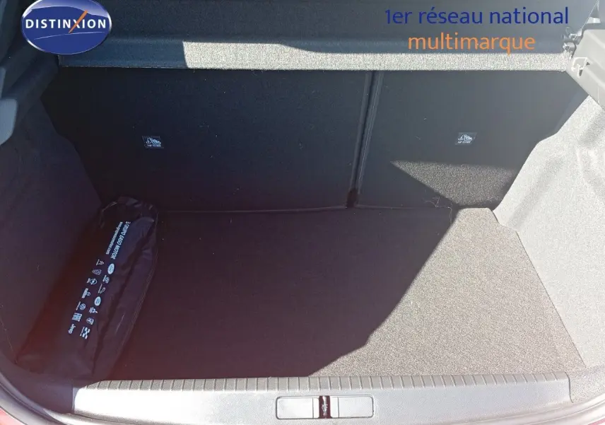 Coffre ouvert d’une Opel Corsa rouge Kardio métal avec toit noir, montrant un espace de chargement vide et un kit de sécurité.