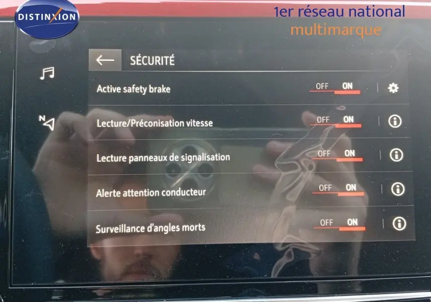 Vue de face rapprochée de l'écran tactile affichant les options de sécurité de l'Opel Corsa rouge Kardio métal avec toit noir.