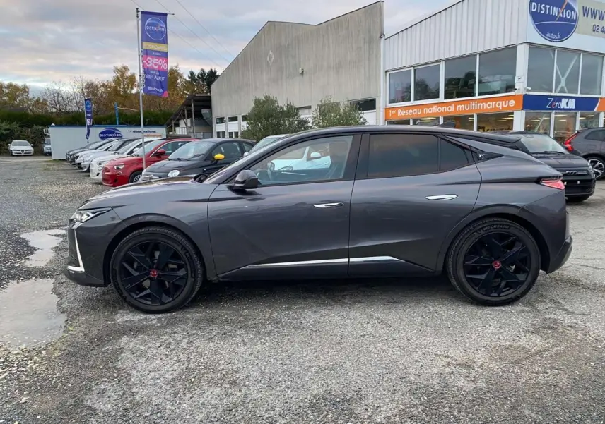 Vue latérale côté gauche d'une DS4 gris platinium 2022 avec jantes noires et lignes épurées, stationnée devant un concessionnaire.