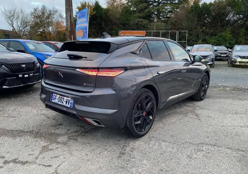 Vue 3/4 arrière droite d'une DS4 gris platinium 2022 avec feux arrière allumés et jantes noires au parking.