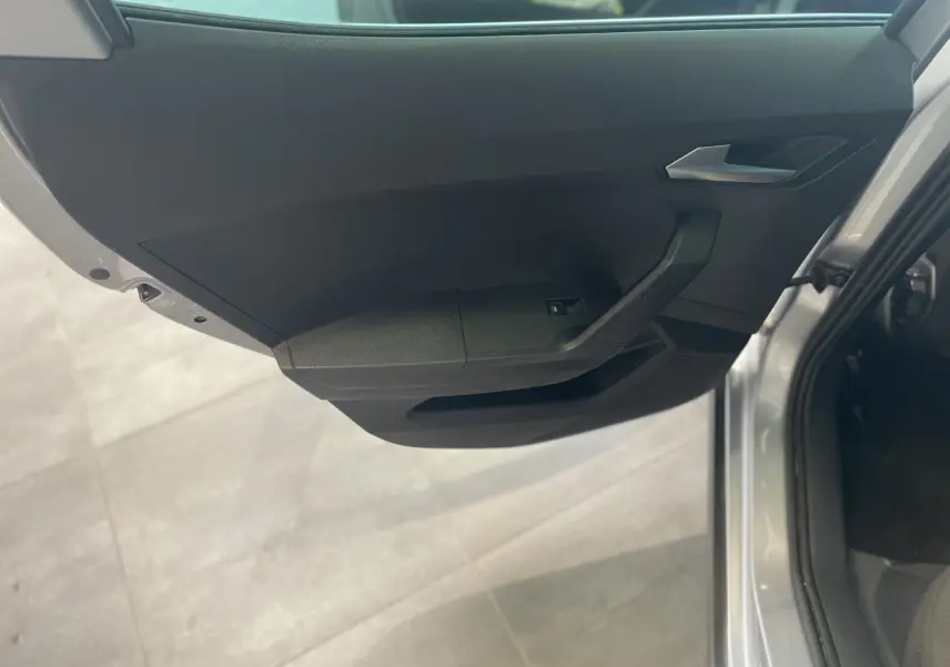 Vue intérieure du panneau de porte avant gauche gris foncé du SEAT Arona 2024 avec poignée argentée et commande de vitre électrique.