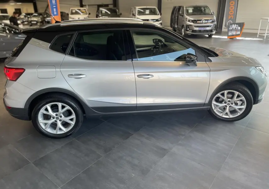 Vue de profil côté gauche du SEAT Arona 2024 en gris clair avec toit noir et jantes alliage 16 pouces en showroom.