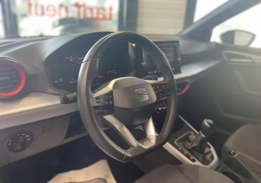 Vue intérieure centrée sur le volant sport cuir noir avec logo SEAT et console centrale d'une Arona FR 2024.