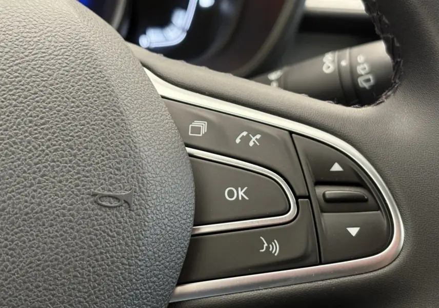 Gros plan sur les commandes au volant cuir noir du Renault Kadjar gris foncé, mettant en valeur les boutons multifonctions.