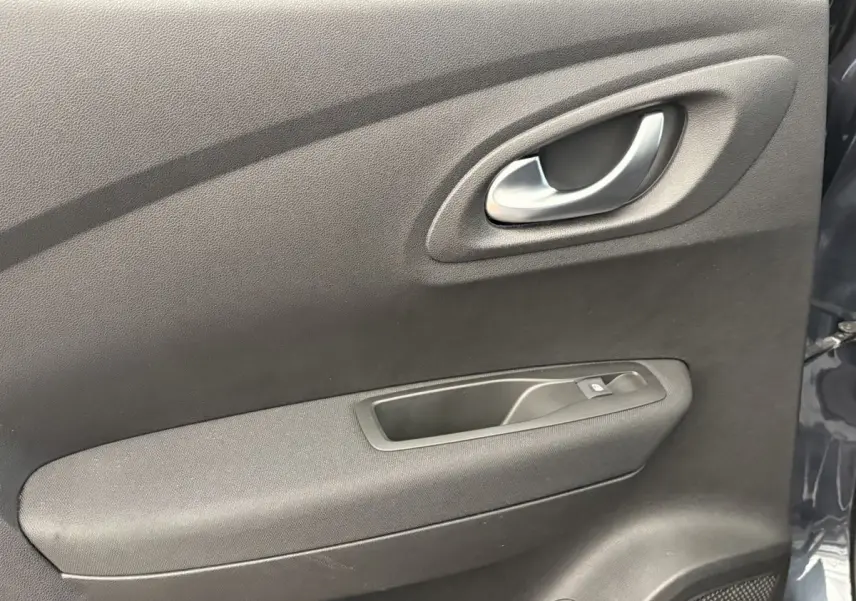 Gros plan sur la porte intérieure côté gauche du Renault Kadjar gris foncé, avec poignée argentée et commande de vitre.