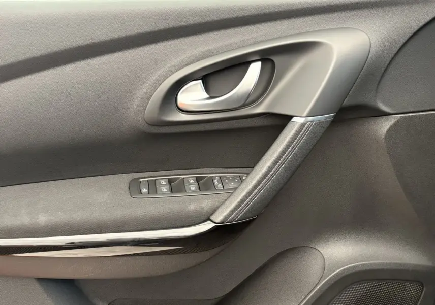 Gros plan sur la porte intérieure côté gauche du Renault Kadjar gris foncé, avec poignée argentée et commandes vitres.