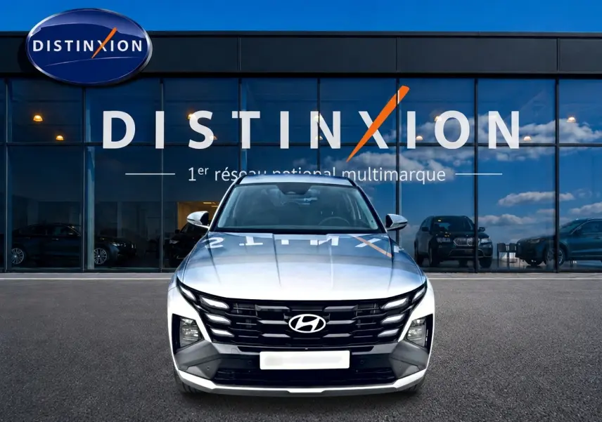 Vue frontale d'un Hyundai Tucson blanc 2026 garé devant une vitrine avec logo Distinxion en reflet.