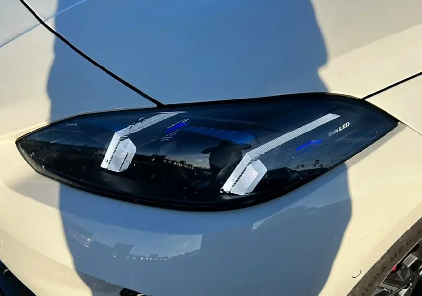 Gros plan sur le phare avant droit LED d'une BMW Série 1 blanche alpin, avec détails lumineux bleus et contours noirs.