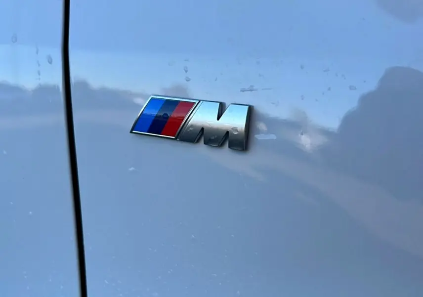 Gros plan sur l'emblème M chromé sur la porte blanche alpin d'une BMW Série 1 2025.