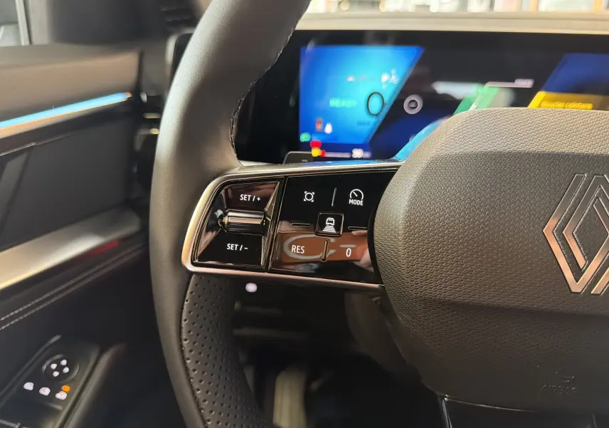 Gros plan sur le volant multifonction noir du Renault Austral E-Tech 200, avec commandes de régulateur et tableau de bord digital flou en arrière-plan.