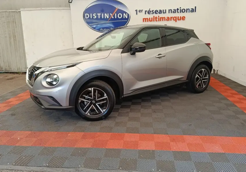 Nissan Juke gris clair vu de profil droit, avec jantes noires et toit noir contrastant, dans un showroom multimarque.