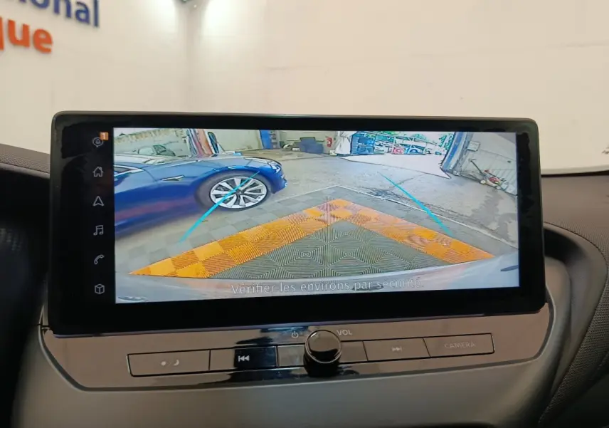 Écran tactile du Nissan Juke 2025 montrant la caméra de recul avec vue sur une voiture bleue à gauche.