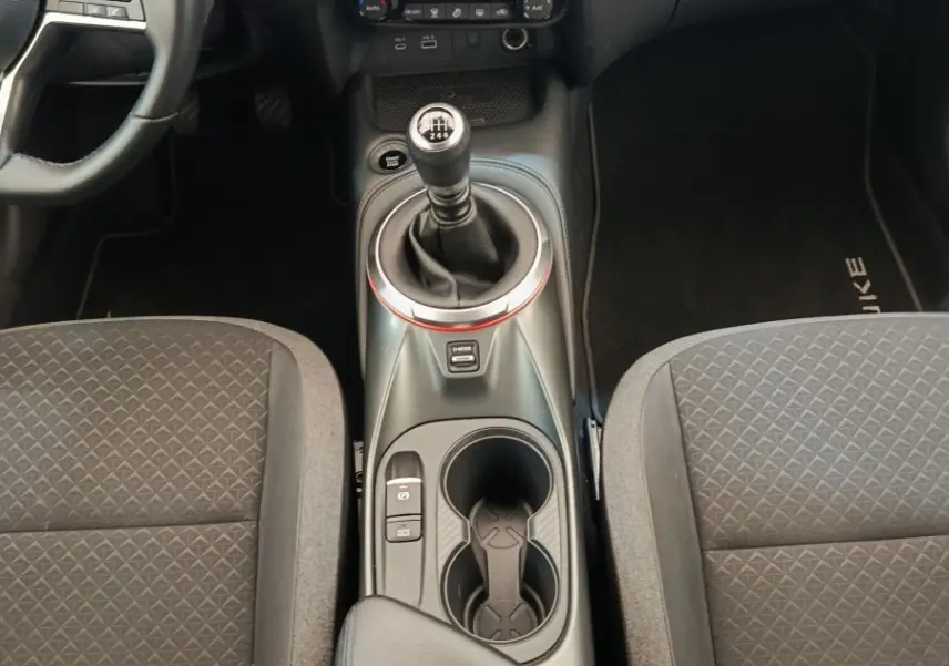 Vue intérieure centrée sur la console centrale et levier de vitesse manuel, sièges tissu gris et volant multifonctions Nissan Juke.