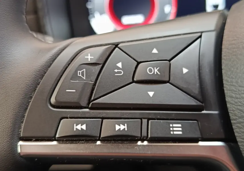 Gros plan sur les commandes multifonctions noires du volant du Nissan Juke 2025, version essence gris clair.