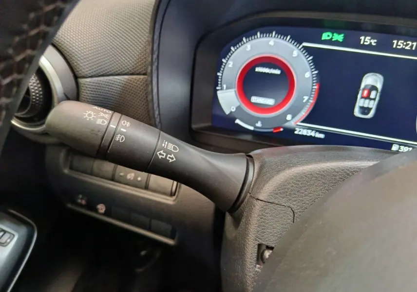 Gros plan sur la manette de clignotants noire à gauche du volant, avec tableau de bord numérique affichant 22 834 km.