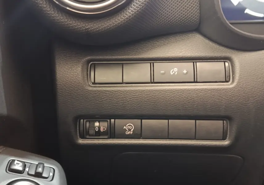 Gros plan sur les commandes de réglage d’éclairage et d’assistance du tableau de bord d’un Nissan Juke gris clair.