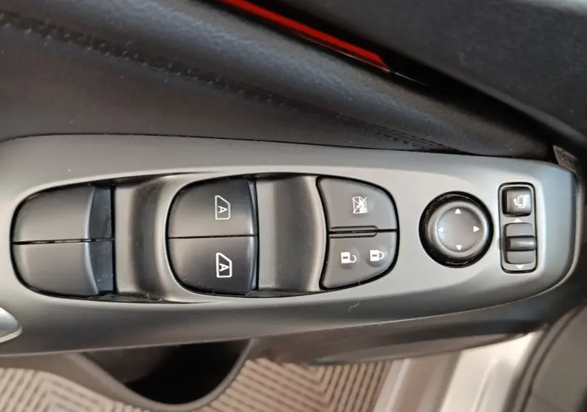 Gros plan sur les commandes de lève-vitres, verrouillage et réglage des rétroviseurs côté conducteur d'un Nissan Juke gris clair.