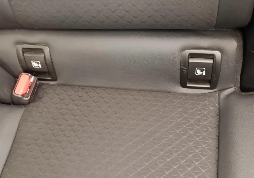 Gros plan sur la banquette arrière gris foncé du Nissan Juke 2025 avec fixation Isofix et boucle de ceinture rouge visible.