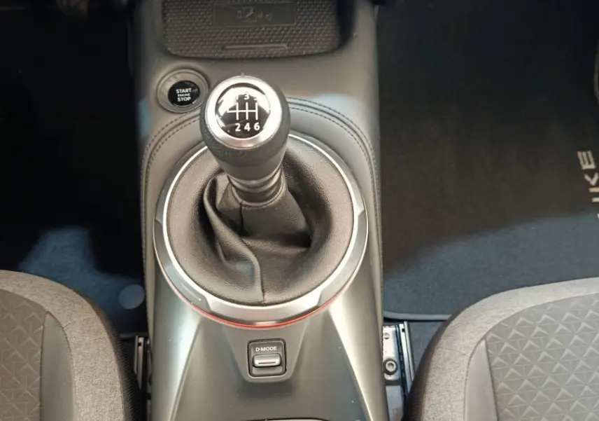Vue rapprochée de la console centrale du Nissan Juke gris clair 2025 avec levier de vitesse manuel et commandes climatisation.