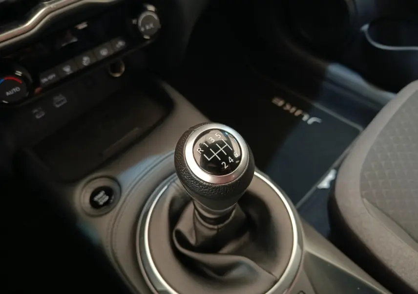 Gros plan sur le levier de vitesses manuel du Nissan Juke gris clair, avec console centrale et tapis marqué Juke visible.